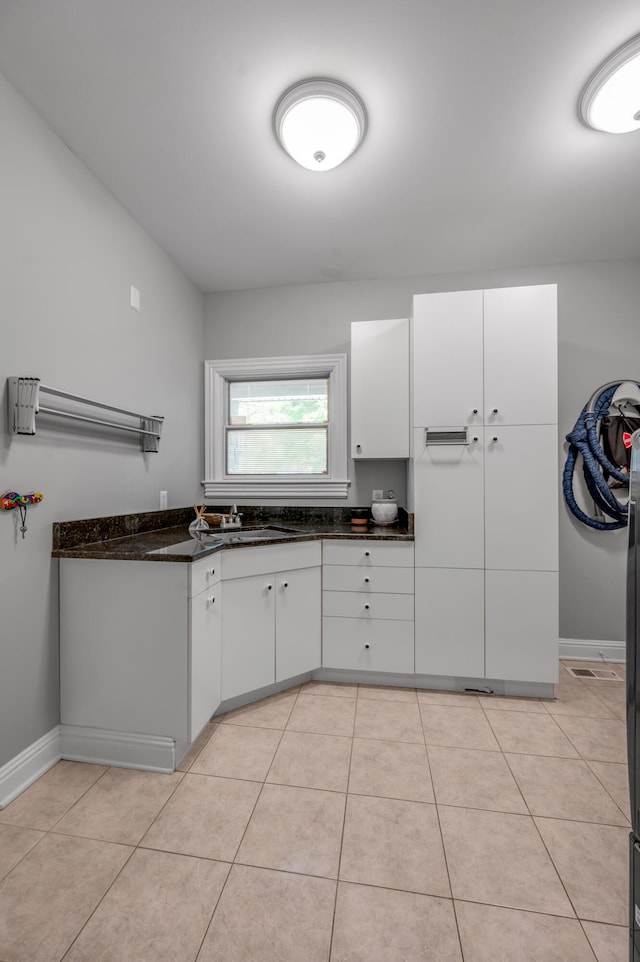 kitchen featuring a sink, baseboards, light tile patterned floors, dark stone counters, and white cabinetry