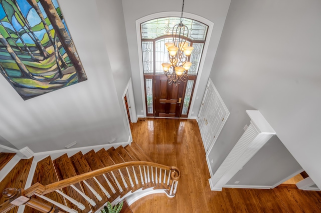 foyer entrance featuring wood finished floors, baseboards, a high ceiling, stairway, and a notable chandelier