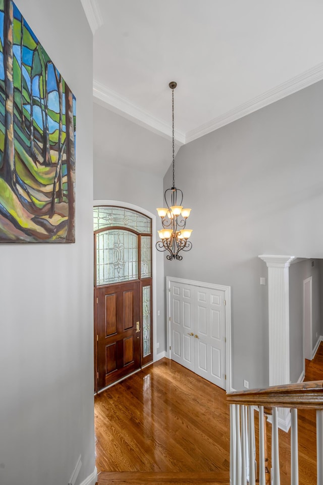 foyer entrance with baseboards, ornamental molding, wood finished floors, and a chandelier