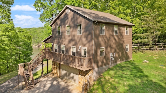 view of side of property featuring a deck with water view, a yard, an attached garage, concrete driveway, and stairs