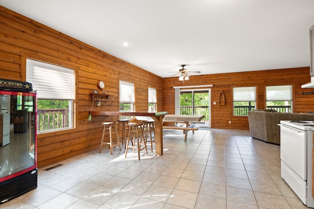 dining room featuring a ceiling fan, wood walls, light tile patterned floors, and a wealth of natural light