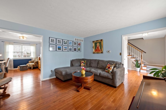 living room with stairs, baseboards, visible vents, and hardwood / wood-style floors