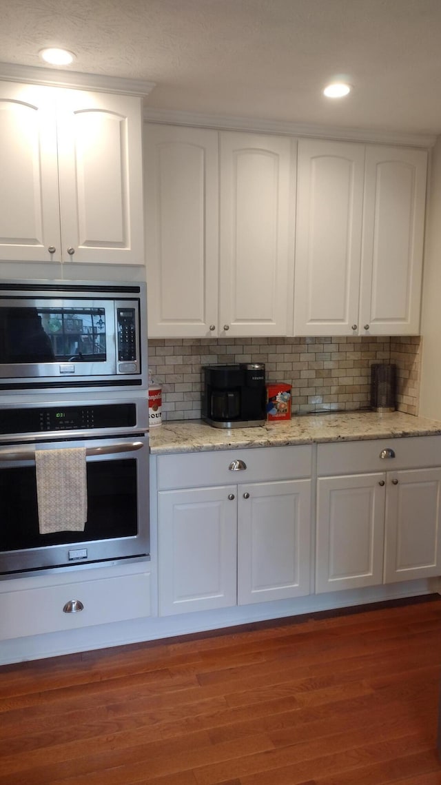 kitchen with white cabinetry, appliances with stainless steel finishes, wood finished floors, and tasteful backsplash