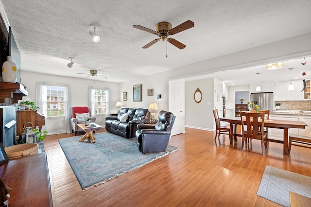 living room with a textured ceiling, ceiling fan, baseboards, and light wood-style floors
