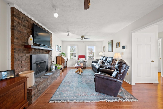 living area with a ceiling fan, a textured ceiling, wood finished floors, and a fireplace