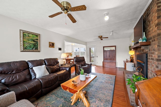 living area featuring a textured ceiling, a brick fireplace, ceiling fan, and wood finished floors