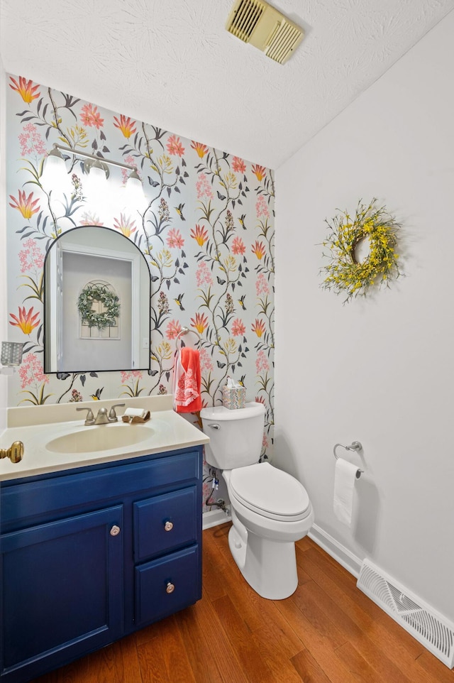 half bath featuring vanity, toilet, wood finished floors, and visible vents