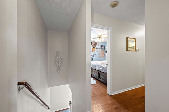 hallway with a textured ceiling, baseboards, an upstairs landing, and wood finished floors