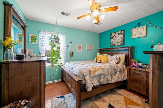 bedroom featuring visible vents, baseboards, a textured ceiling, and wood finished floors