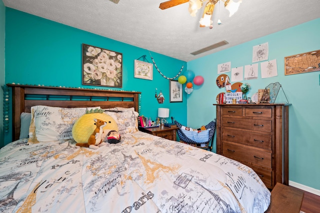 bedroom with visible vents, wood finished floors, baseboards, a textured ceiling, and a ceiling fan