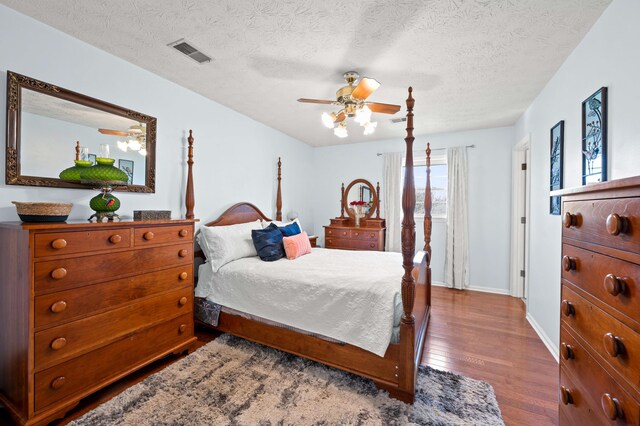 bedroom featuring visible vents, baseboards, ceiling fan, a textured ceiling, and dark wood finished floors