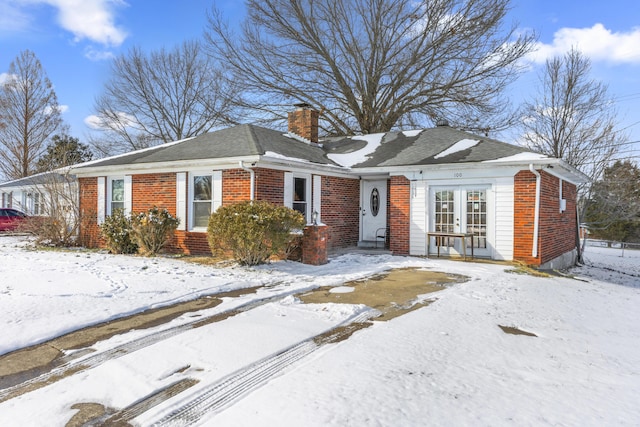 view of front facade with brick siding, french doors, and a chimney
