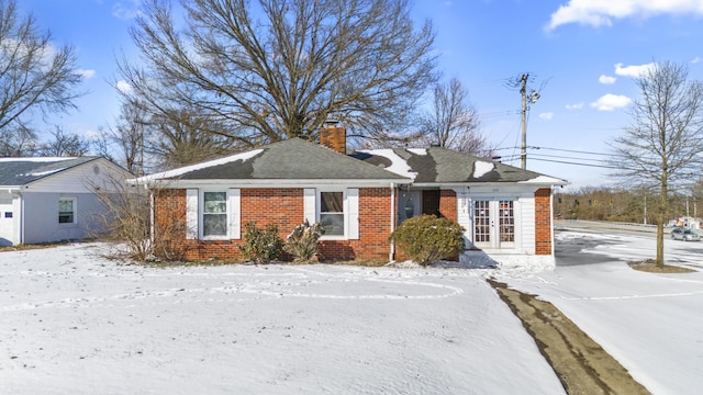 bungalow-style house with french doors, a chimney, and brick siding