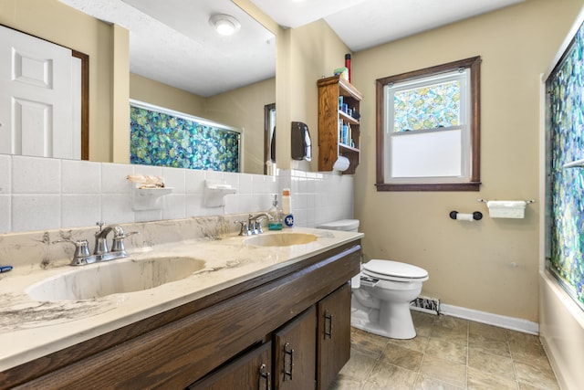 bathroom with a sink, baseboards, toilet, and double vanity