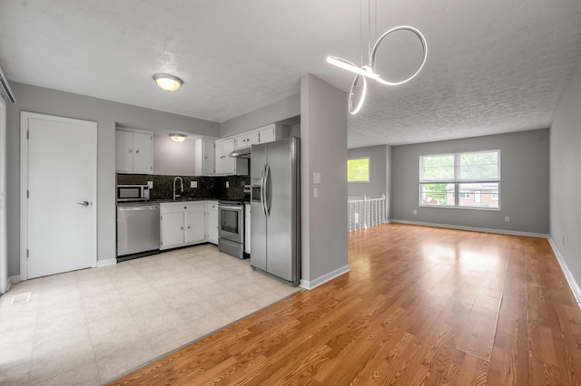 kitchen featuring stainless steel appliances, a sink, tasteful backsplash, white cabinetry, and baseboards