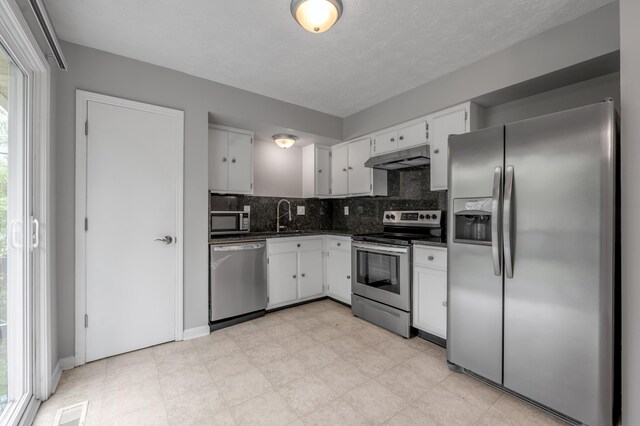 kitchen with appliances with stainless steel finishes, dark countertops, under cabinet range hood, and white cabinets