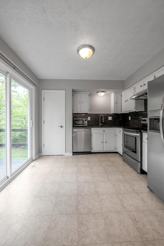 kitchen with stainless steel appliances, under cabinet range hood, a sink, tasteful backsplash, and white cabinetry
