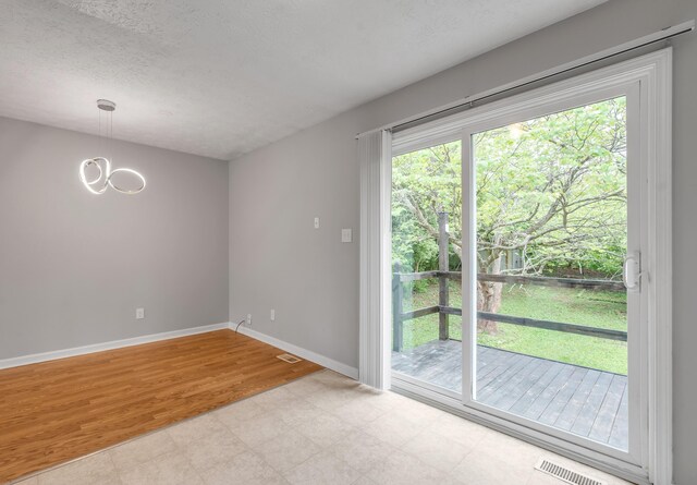 empty room with baseboards, a chandelier, light flooring, and a textured ceiling