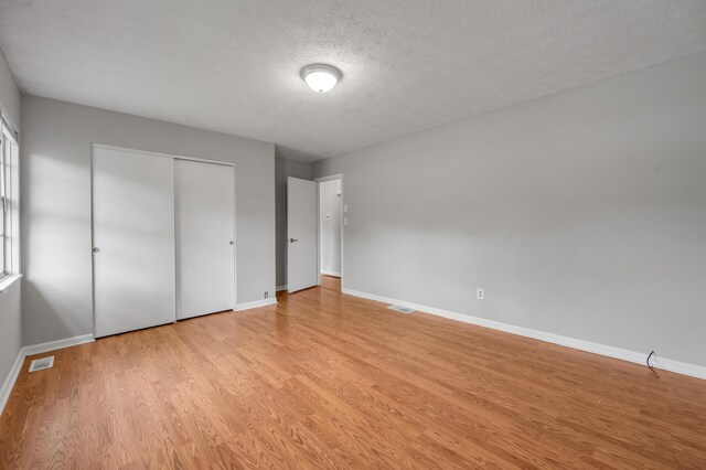 unfurnished bedroom featuring baseboards, light wood finished floors, a closet, and a textured ceiling