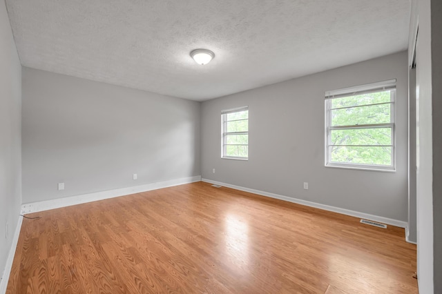 empty room with light wood-style flooring, a textured ceiling, and baseboards