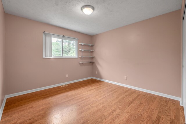 unfurnished room featuring light wood-type flooring, baseboards, and a textured ceiling