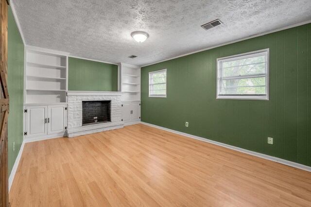 unfurnished living room with light wood-style floors, a fireplace, baseboards, built in features, and a textured ceiling