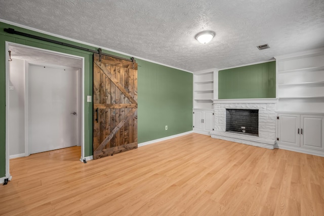 unfurnished living room with wood finished floors, crown molding, a textured ceiling, a stone fireplace, and baseboards