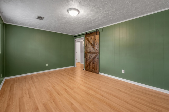 unfurnished room featuring a barn door, wood finished floors, a textured ceiling, and baseboards