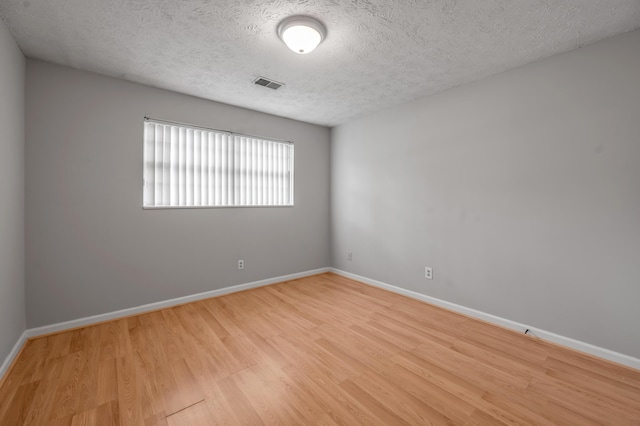 spare room with light wood finished floors, a textured ceiling, and baseboards