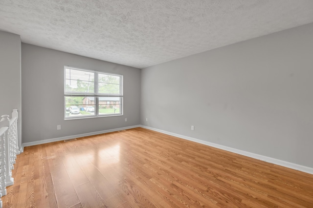 spare room with light wood-style floors, baseboards, and a textured ceiling