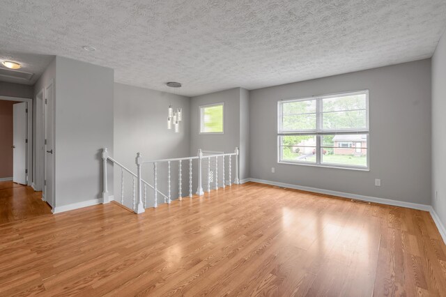 unfurnished room with light wood-style floors, baseboards, and a textured ceiling