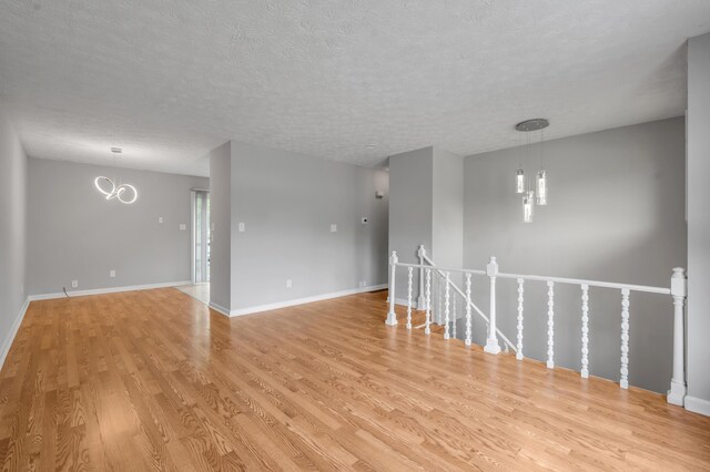 unfurnished room featuring light wood-type flooring, a chandelier, a textured ceiling, and baseboards