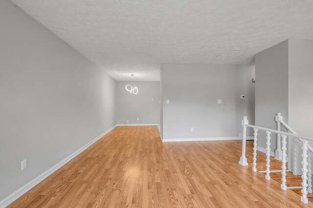 empty room with light wood-type flooring, a textured ceiling, and baseboards