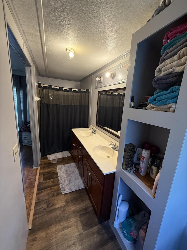 full bath featuring double vanity, wood finished floors, a textured ceiling, a shower with curtain, and a sink