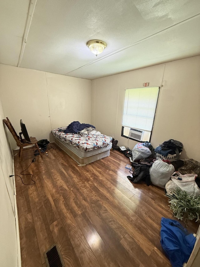bedroom featuring a textured ceiling, cooling unit, wood finished floors, and visible vents