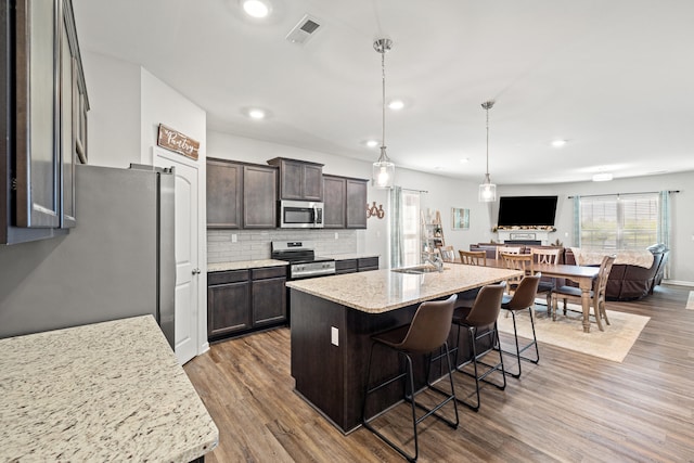 kitchen with dark brown cabinets, stainless steel appliances, open floor plan, wood finished floors, and visible vents
