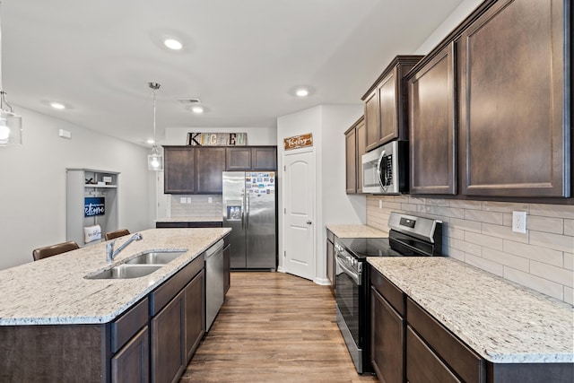 kitchen with a kitchen island with sink, backsplash, appliances with stainless steel finishes, dark brown cabinets, and a sink
