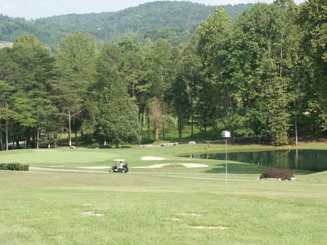 view of home's community with a water and mountain view, a lawn, and golf course view