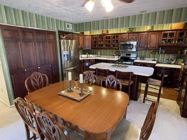 dining room featuring a textured ceiling, wallpapered walls, light colored carpet, and ceiling fan