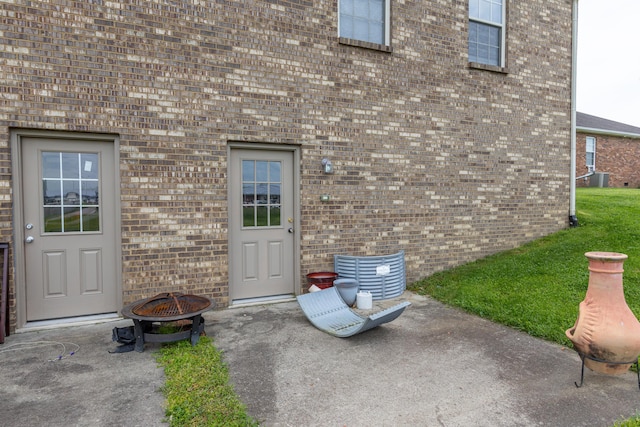 view of exterior entry with a lawn, brick siding, and a patio area