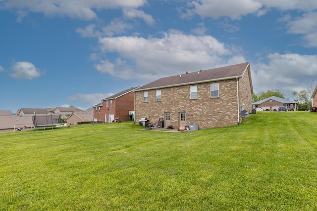 back of house featuring a lawn, a trampoline, and brick siding