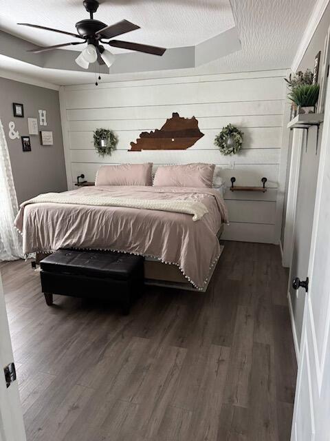 bedroom featuring wooden walls, ceiling fan, dark wood-style flooring, and a textured ceiling