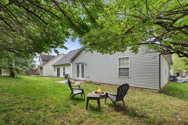 rear view of house featuring french doors, a lawn, a fire pit, and cooling unit