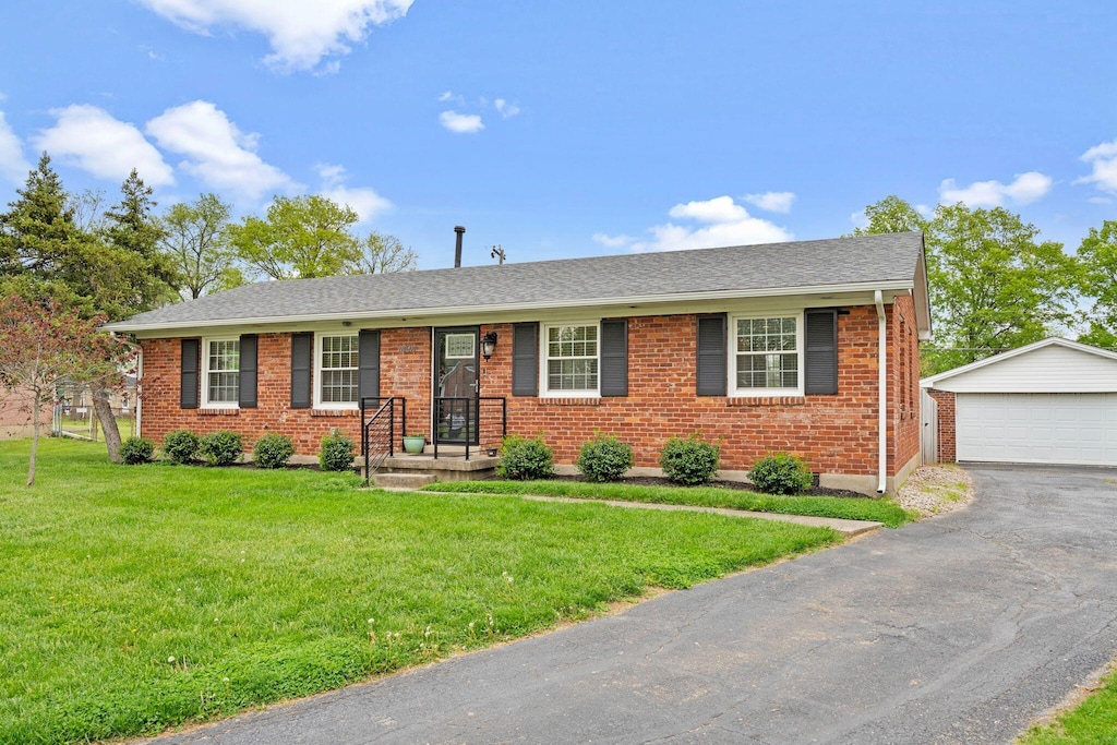 single story home featuring brick siding, a front lawn, an outbuilding, and a detached garage