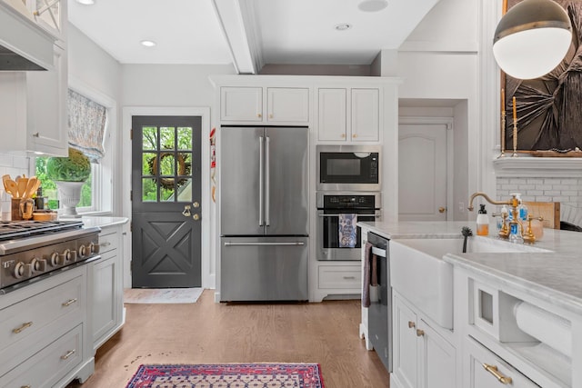 kitchen featuring backsplash, appliances with stainless steel finishes, a sink, white cabinets, and beamed ceiling
