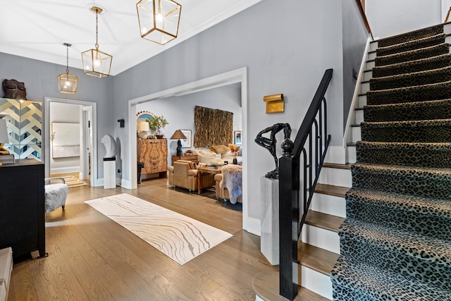entrance foyer featuring crown molding, stairs, wood finished floors, baseboards, and a chandelier