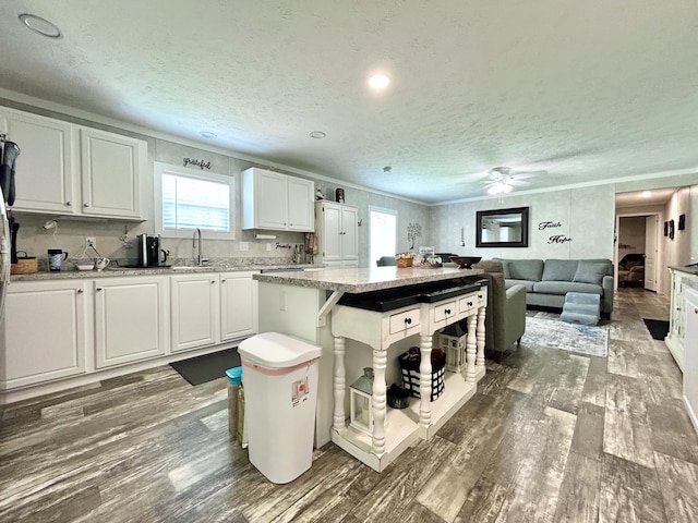 kitchen with white cabinets, light stone counters, a sink, a textured ceiling, and wood finished floors