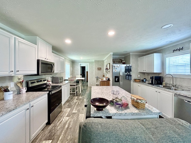 kitchen with white cabinets, stainless steel appliances, a sink, and light wood-style flooring