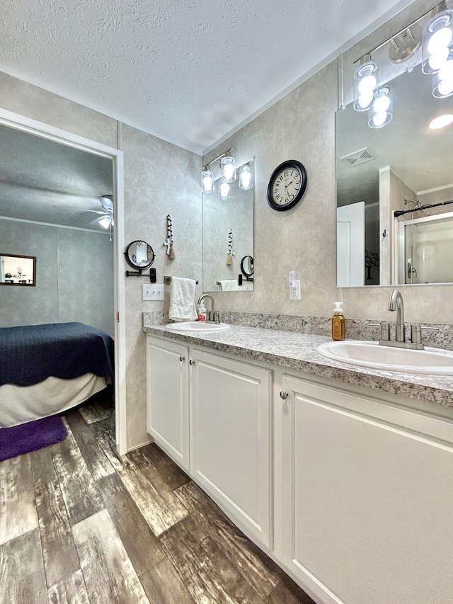 full bathroom with a sink, a textured ceiling, double vanity, and wood finished floors