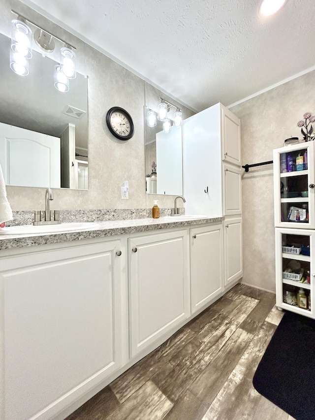 bathroom featuring double vanity, a textured ceiling, a sink, and wood finished floors
